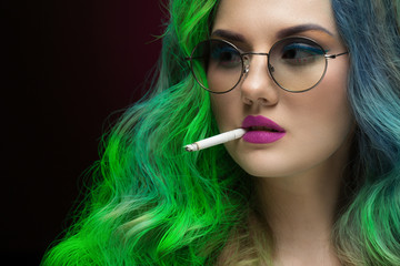 Obraz premium Smoking woman. Closeup shot of a beautiful woman with colorful hair wearing glasses smoking a cigarette looking away on black background
