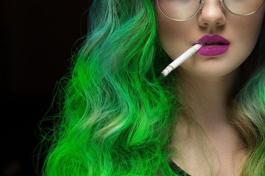 Fierce lady. Cropped closeup of a green haired female fashion model wearing purple lipstick holding a cigarette between her lips