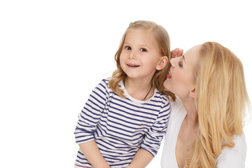 Can not believe. Studio shot of a cheerful mother whispering secrets to her surprised little daughter isolated on white.