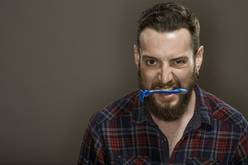 Power of beard. Studio shot of a furious bearded guy holding a razor in his mouth looking to the camera copyspace on the side.