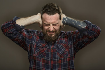 Searching for silence. Portrait of a bearded stressed man covering his ears with his hands on grey background.