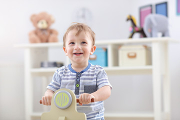 Cheerful baby boy swinging on a rocking chair in the shape of a scooter
