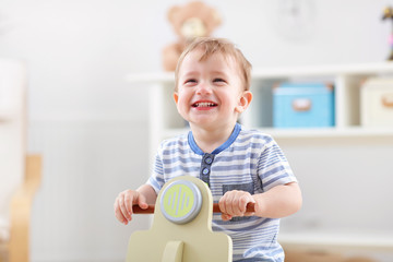 Cheerful baby boy swinging on a rocking chair in the shape of a scooter