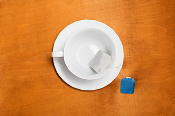 White cup with a tea bag with a blue label on an orange wooden table on top
