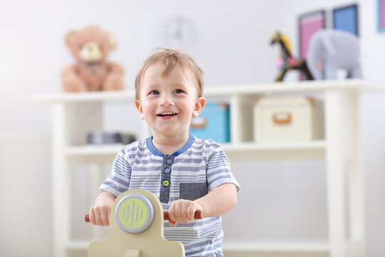 Cheerful Baby Boy Swinging On A Rocking Chair In The Shape Of A Scooter