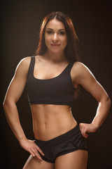 Obraz premium Confident in her success. Vertical studio shot of a sporty brunette wearing black top and shorts posing looking to the camera against black background.