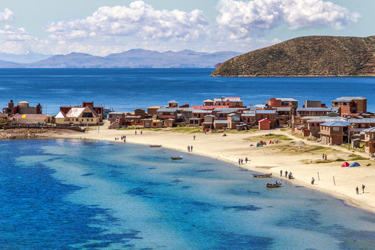 Blue water and coast of Titicaca lake, boats, walking people and bolivian village at Incas Island of the Sun, Bolivia, south America