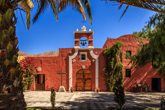 Red walls of Spanish catholic chapel with palms, trees and flowers, Arequipa, Peru