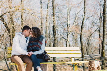 Happy couple in love hugging and sharing emotions, holding hands on a bench by the river
