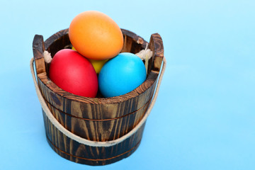painted easter colorful eggs in wooden bucket on blue background