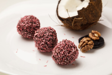 Candies in coconut flakes and fresh coconut on white plate