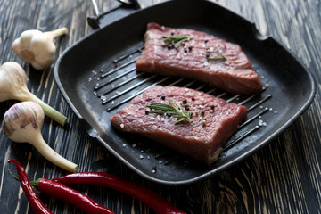 raw steak on cast iron frying pan with garlic and pepper.