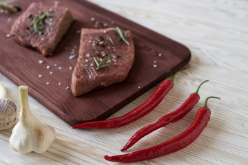 Fresh raw steaks with rosemary, pepper and garlic on wooden desk