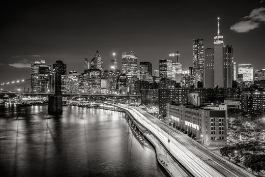 Fototapeta Lower Manhattan skyscrapers and Financial District. The Black & White elevated night view includes the West tower of the Brooklyn Bridge, East River and traffic light trails on the FDR Drive. New York