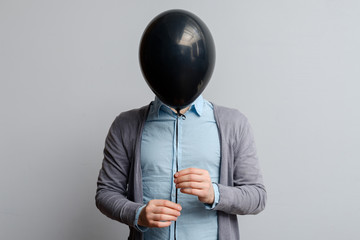 A white man covers his face with a black balloon. Hiding from problems