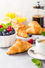 Delicious continental breakfast with fresh flaky croissants, assorted preserves, ripe berries, orange juice and coffee, close up on the croissant.