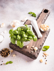 Ingredients for making green pesto sauce. Basil in white mortar on wooden cutting board. Healthy italian food. Retro style toned. High angle view.