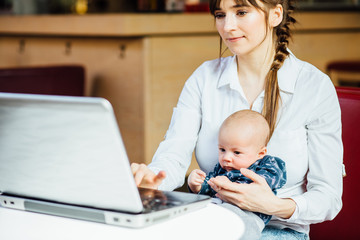 Young female student - mother siting in cafe with newborn baby on her hands and working in tablet laptop. Motherhood, Study, Work and Lifestile concept.