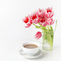 Fototapeta na wymiar Tulips in glass and coffee cup on white table.