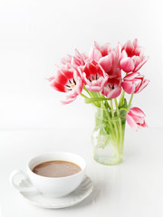 Fototapeta na wymiar Tulips in glass and coffee cup on white table.