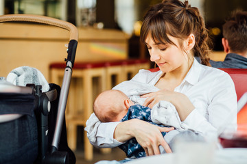 A young mother is breastfeeding her baby in a cafe while she is having a tea time