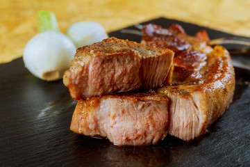 Grilled pork steaks on black stone background.