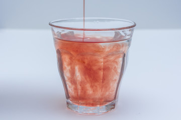fruit juice extract poured into glass of water on white background