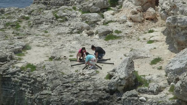 Portable dance spinning pole kit assembly and installation on a cliff. Young women dancers installing dancing pole for fitness exercise on a rock by the sea.