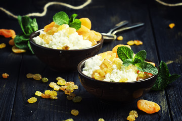 Homemade cottage cheese with dried apricots, raisins and mint in clay bowls, healthy breakfast, dark background, selective focus