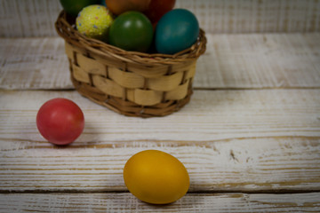 Colored easter eggs in basket on wooden background