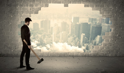 Business man hitting wall with hammer on city view