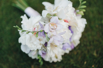 Wedding rings of the bride and groom lie on a bouquet of flowers and greens