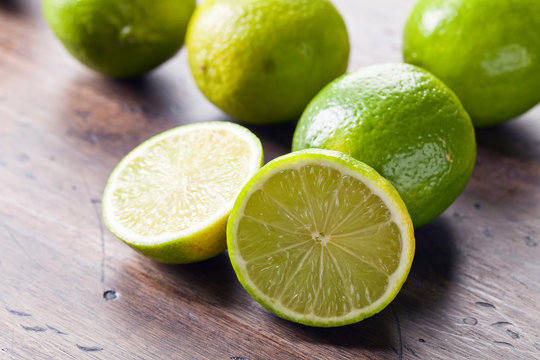 Group of whole and cut fresh limes on a wooden table .