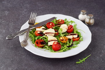 Traditional Italian salad with cherry tomato, ruccola, mozzarella, olive oil wine vinegar on a white plate on a grey abstract background.