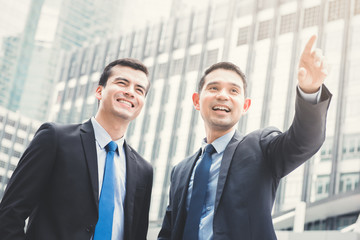 Fototapeta premium Two businessmen standing outdoors in the city with one hand pointing out