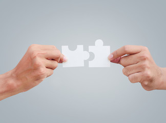 Cropped hands of businessmen joining jigsaw pieces on gray background