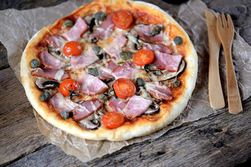 Homemade pizza with smoked meat, ham, mushrooms, cherry tomato, capers and cheese.