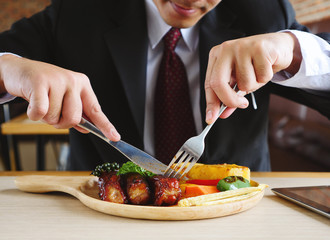 Happy young businessman eating rib steak on wooden tray at restaurant
