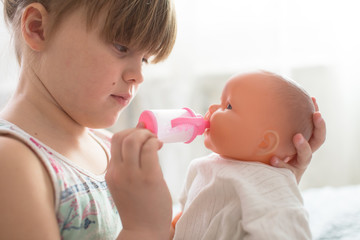 Kid girl playing with doll, feeding doll bottle
