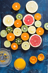 Freeshly squeezed juice and fruits rich in vitamin C: oranges, lemons, kiwis, grapefruits and limes on the black slate on the dark blue background, top view