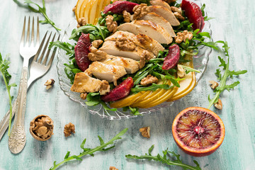 Fresh spring salad with grilled chicken breast, arugula, pear and orange slices and walnuts on wooden table. Selective focus