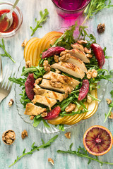 Fresh spring salad with grilled chicken breast, arugula, pear and orange slices and walnuts on wooden table. Selective focus