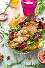 Fresh spring salad with grilled chicken breast, arugula, pear and orange slices and walnuts on wooden table. Selective focus