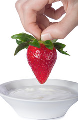 Female hand dipping ripe fresh strawberry into a cup of yogurt