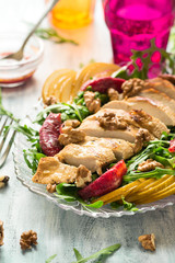 Fresh spring salad with grilled chicken breast, arugula, pear and orange slices and walnuts on wooden table. Selective focus