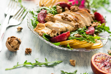 Fresh spring salad with grilled chicken breast, arugula, pear and orange slices and walnuts on wooden table. Selective focus