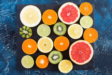 Fruits rich in vitamin C: oranges, lemons, kiwis, grapefruits and limes on the black slate on the dark blue background, top view