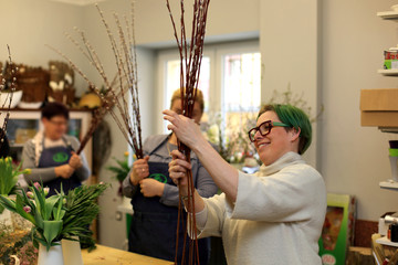 Uśmiechnięta kobieta pokazuje robienie palmy Wielkanocnej w kwiaciarni. - obrazy, fototapety, plakaty
