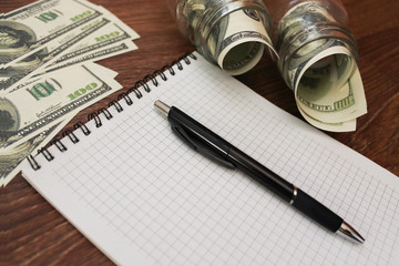 Business concept. Financial analysis and money in US dollars, the concept of saving money, glass jars with money, notepad and pen on the wooden background