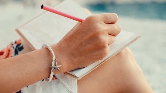 Close up view of a woman writing in her diary at sunset sitting on the beach